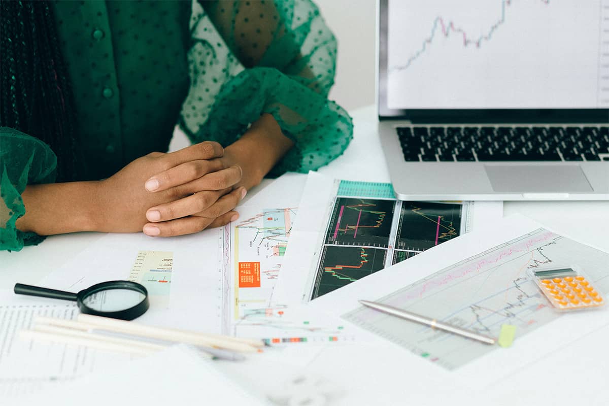 A woman in a green shirt sits at a desk examining papers with graphs and analytics.